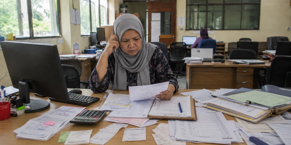 Administrator reviewing manual canteen reports and paper records in an office