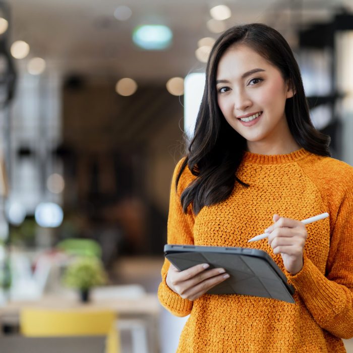 smart confidence asian female startup entrepreneur small business owner businesswoman wear smart casual cloth smile hand use tablet woking inventory checking in showroom office daytime background